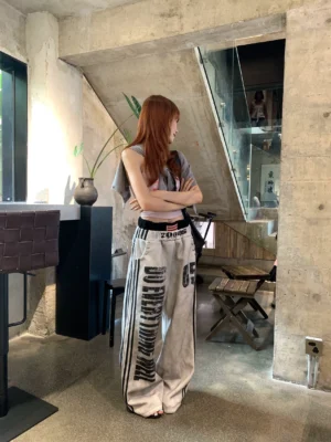 Side full-body view of washed gray Y2K grunge slogan track pants with ultra-wide stacked legs, black racing stripes, 2000S waistband, and DO EVERYTHING WELL graphic styled with cropped streetwear outerwear