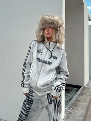 Model wearing a washed white Y2K grunge track jacket with black sleeve stripes, skull graphic, high collar, and matching wide-leg track pants on an industrial rooftop