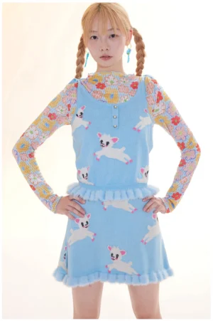 Front full-body view of a light blue lamb print knit cami and ruffle mini skirt set styled with a layered long-sleeve top