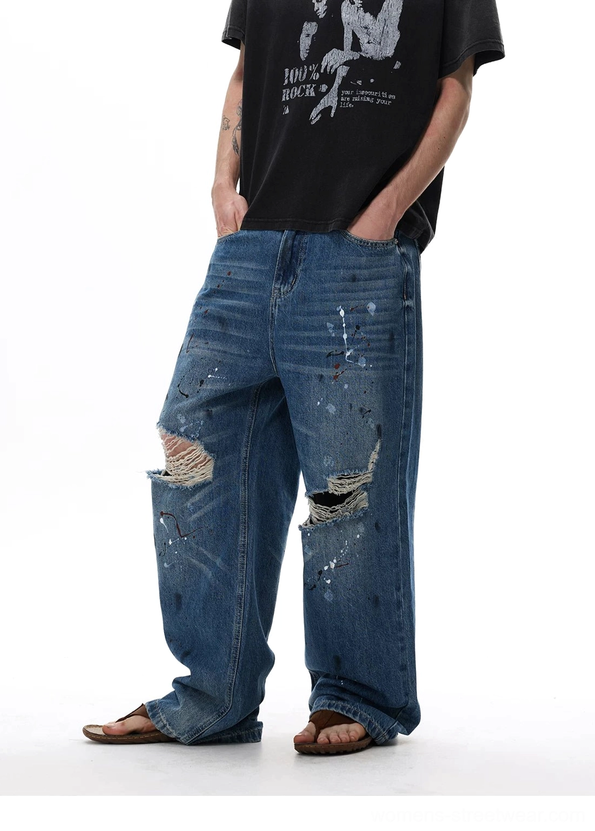 Three-quarter front view of loose paint splatter denim jeans with multiple distressed knee rips and Y2K streetwear attitude