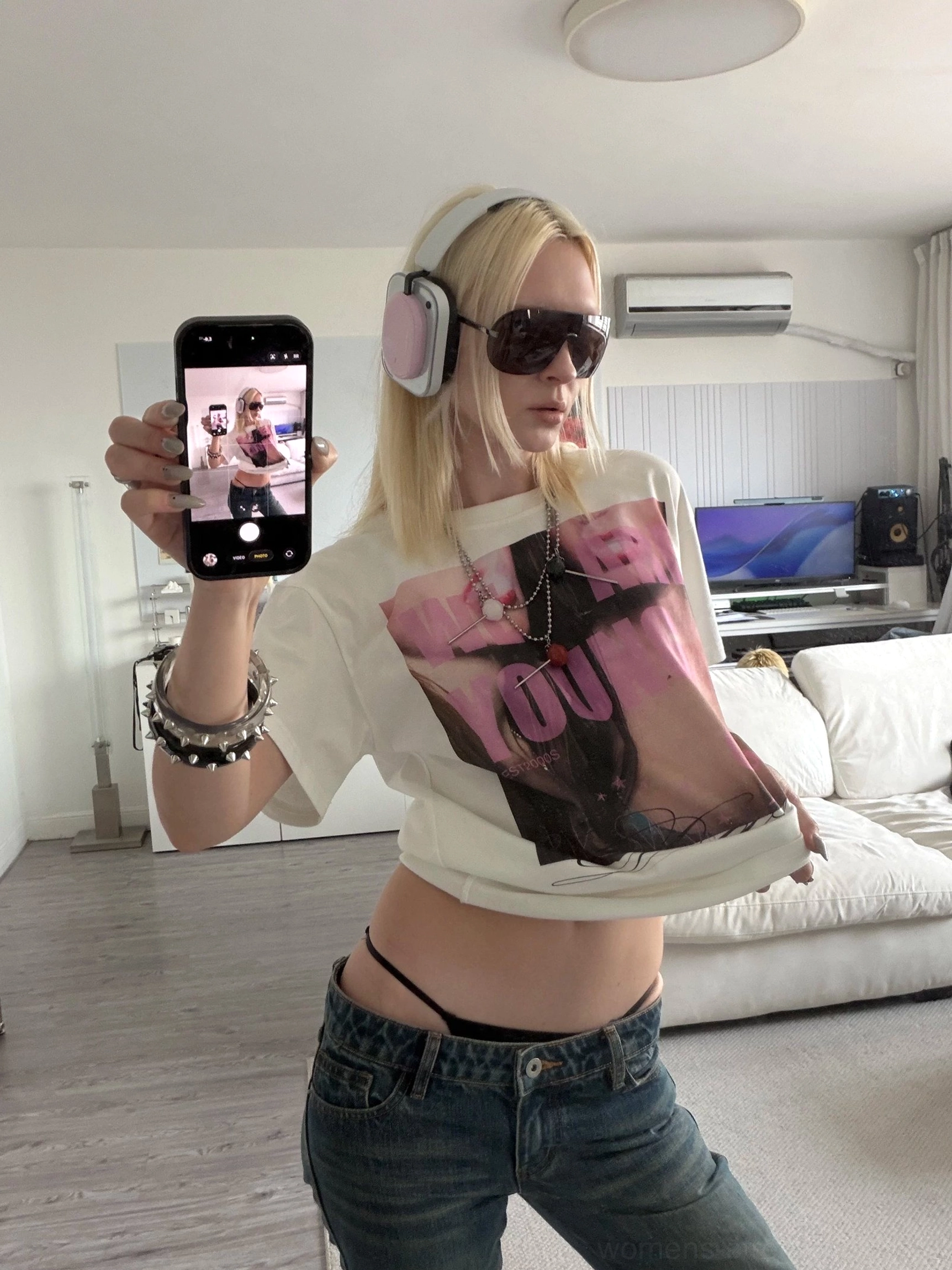 Model wearing a white Y2K graphic T-shirt with pink portrait artwork and We Are Young lettering styled with low-rise blue jeans