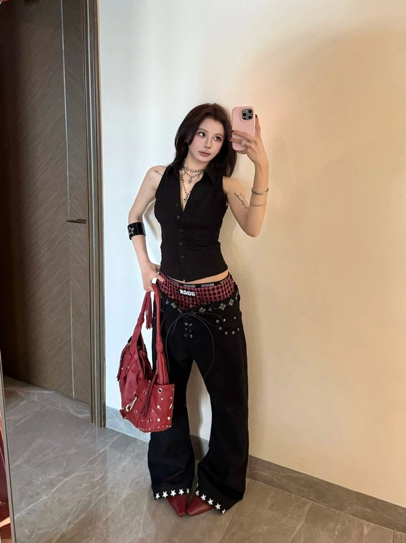 Front mirror selfie showing Y2K punk wide leg black jeans with red plaid double waistband, star rivet trim, and oversized streetwear silhouette