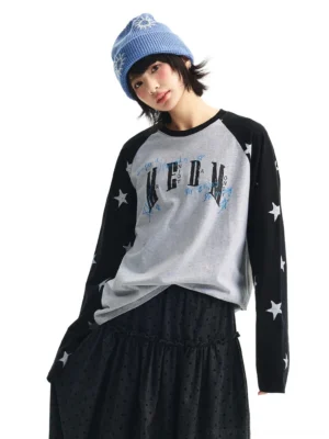 Female model wearing a black and gray star print raglan graphic long sleeve streetwear T-shirt with a blue beanie and black midi skirt