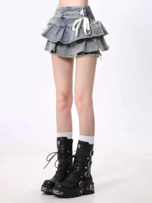 Front close-up of a washed light blue Y2K ruffled mini skirt with front ribbon bow ties, double layered frayed hem, white socks, and black platform combat boots