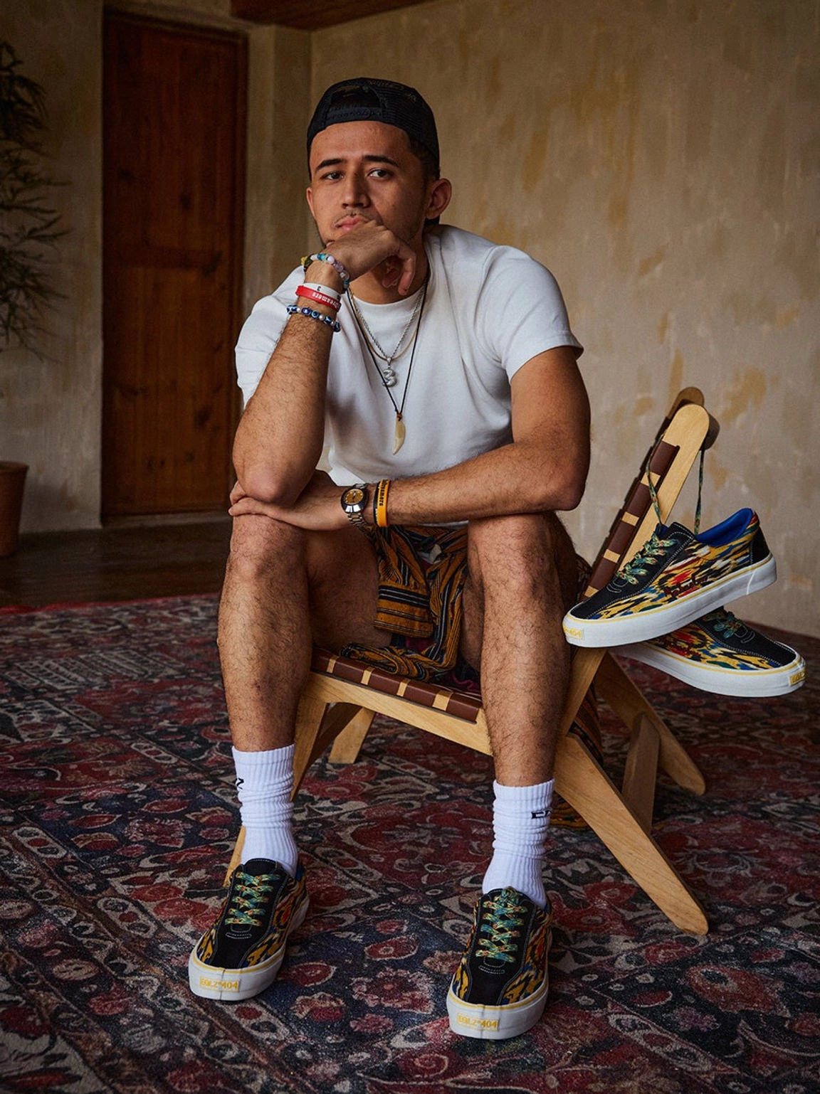 Front three-quarter view of yellow abstract print skate shoes worn with patterned shorts in retro indoor setting