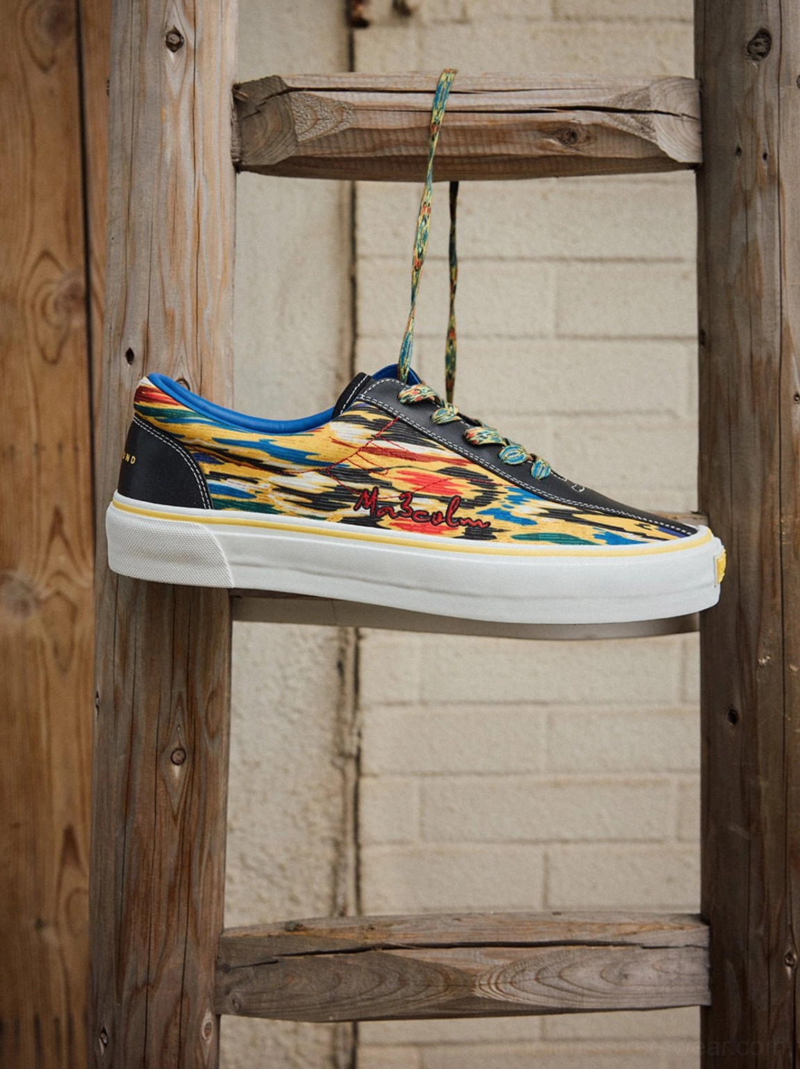 Hanging side profile of yellow abstract print canvas skate shoes showing black toe trim and white sole