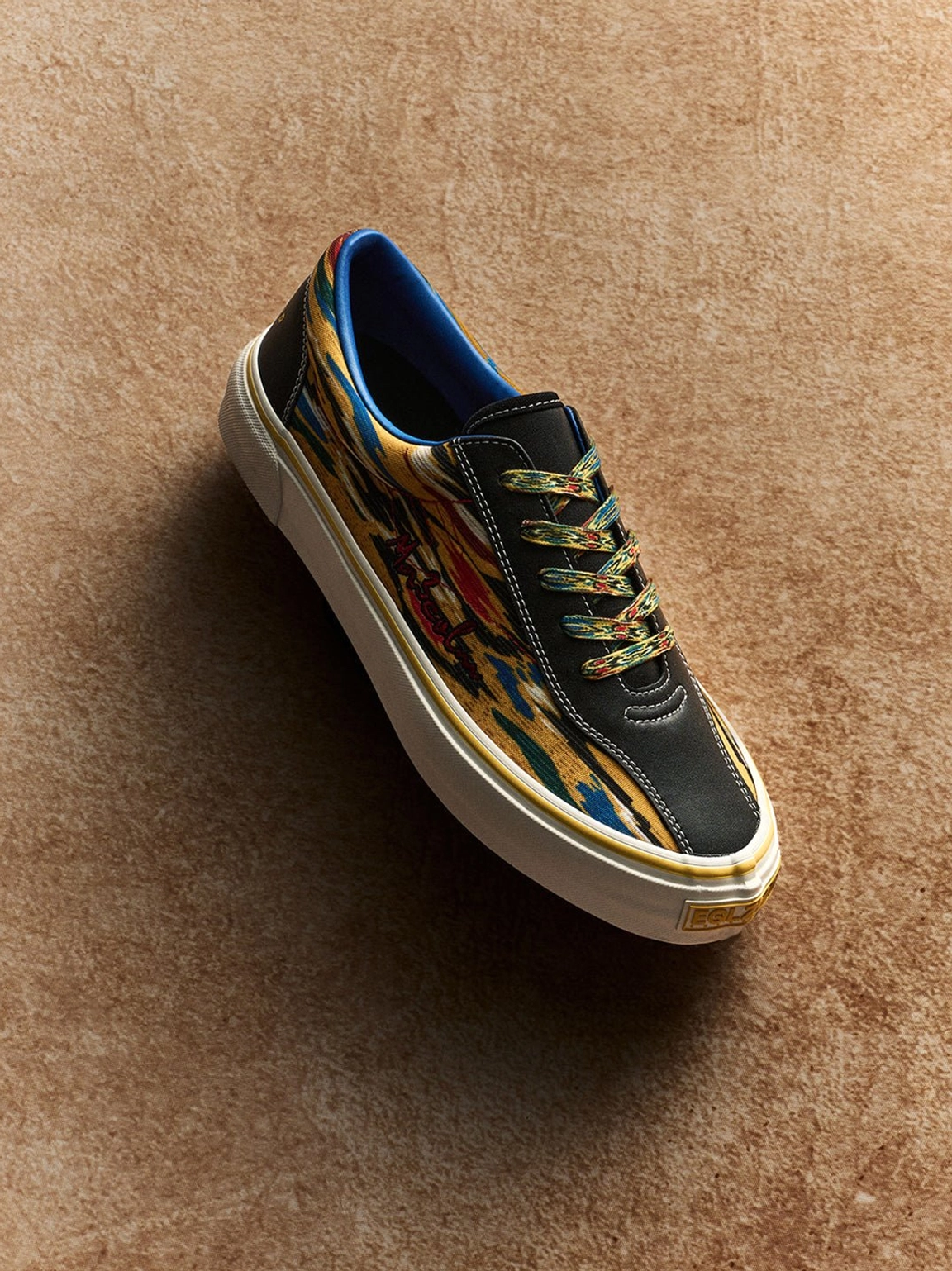 Top view close-up of colorful abstract print canvas skate shoes with yellow laces, black trim, and blue lining