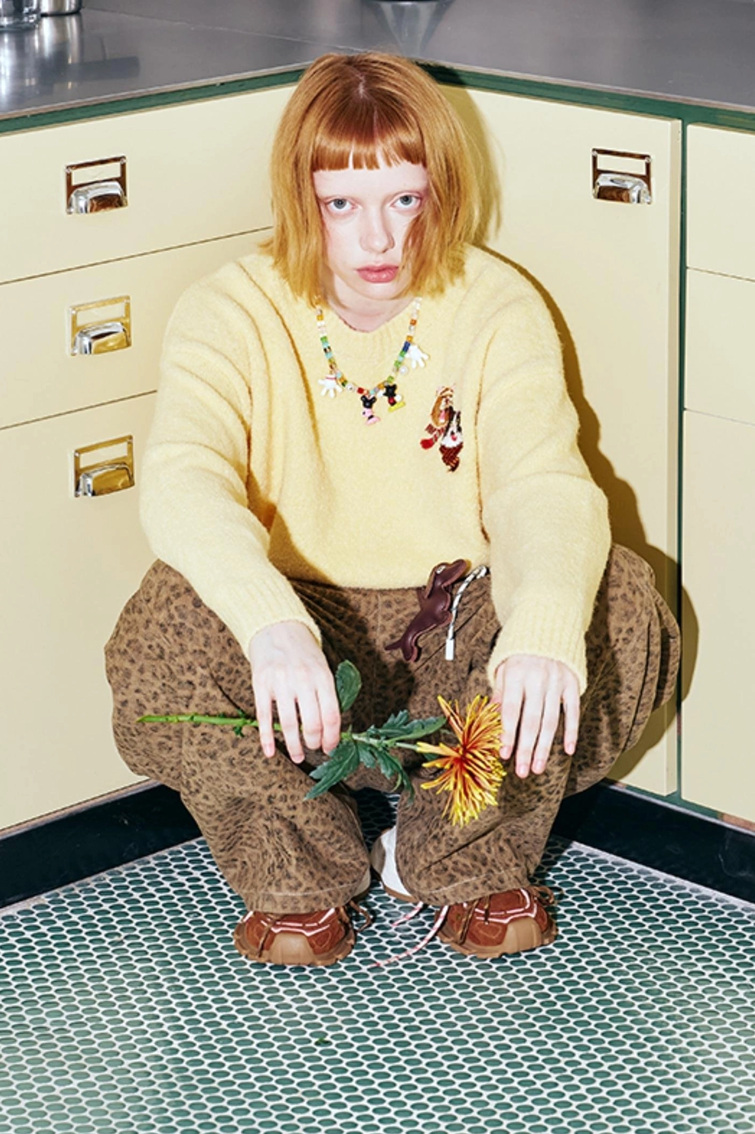 Low-angle styling view of yellow cat knit sweater with beaded necklace leopard print pants and brown shoes