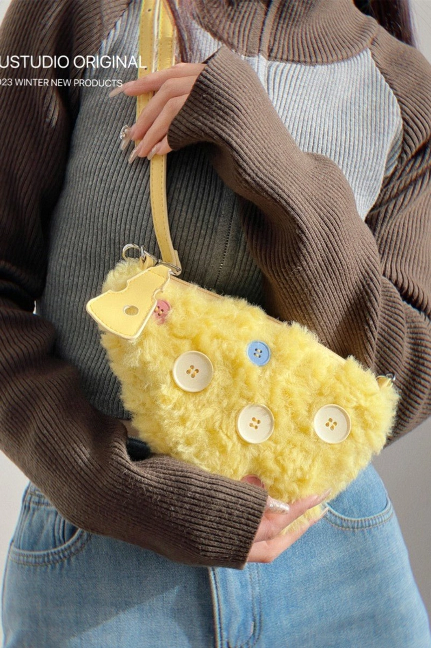Close-up of hands holding yellow cheese-style fuzzy shoulder bag showing soft plush surface and colorful button details