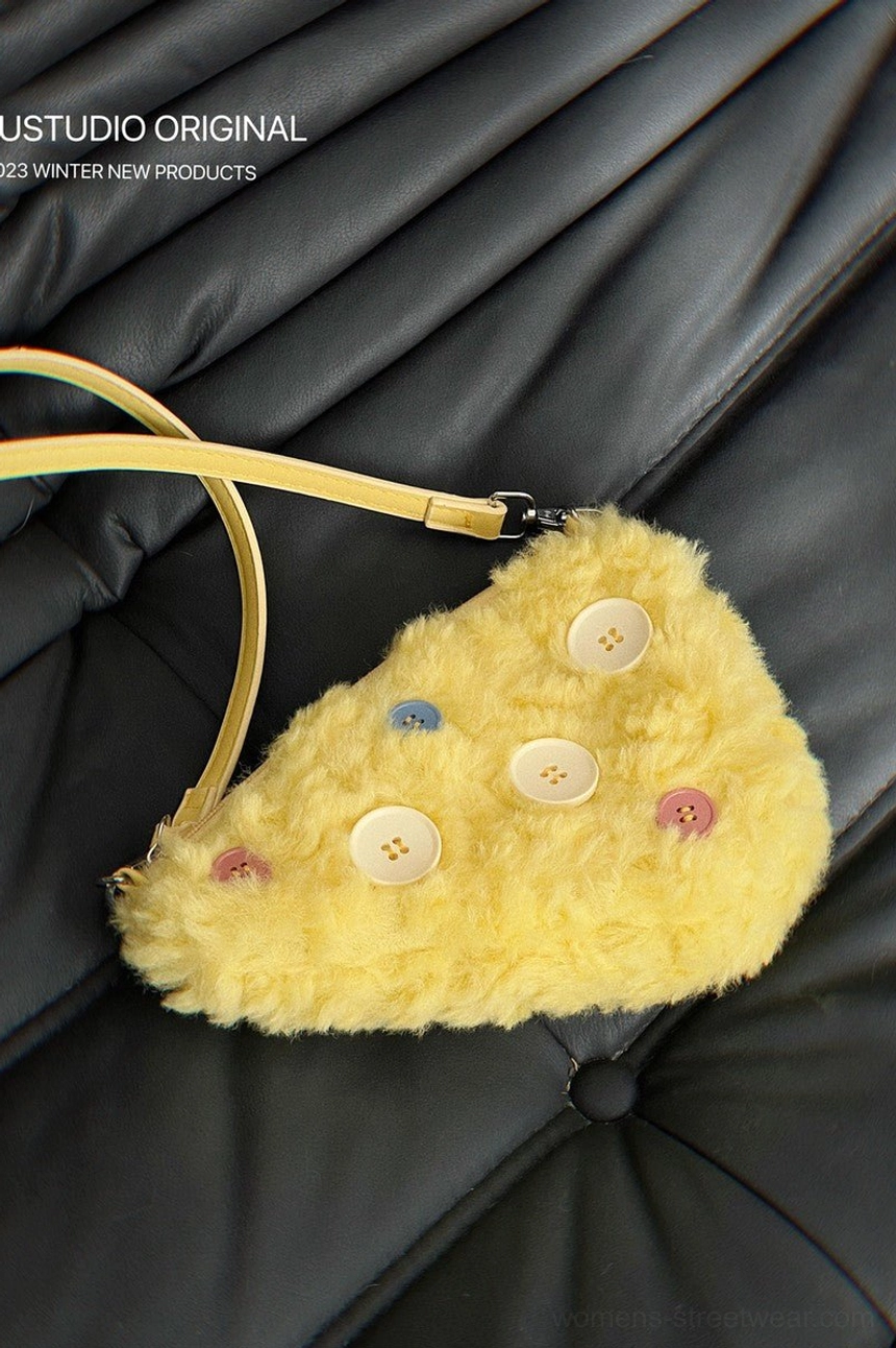 Yellow cheese-shaped fuzzy mini shoulder bag flat lay on black leather sofa showing colorful buttons and yellow strap