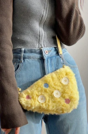 Yellow cheese fuzzy button mini shoulder bag worn at the hip with color-block knit top and blue denim jeans