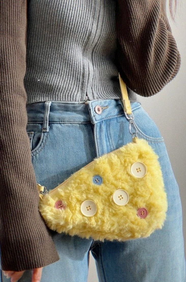 Yellow cheese fuzzy button mini shoulder bag worn at the hip with color-block knit top and blue denim jeans