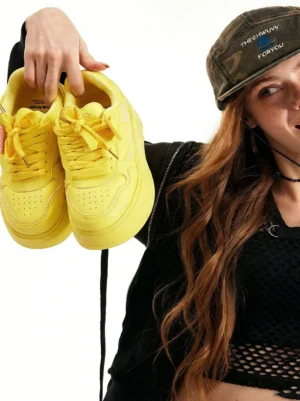 Female streetwear model holding yellow Cupid heart platform sneakers with pink heart-shaped lace accents