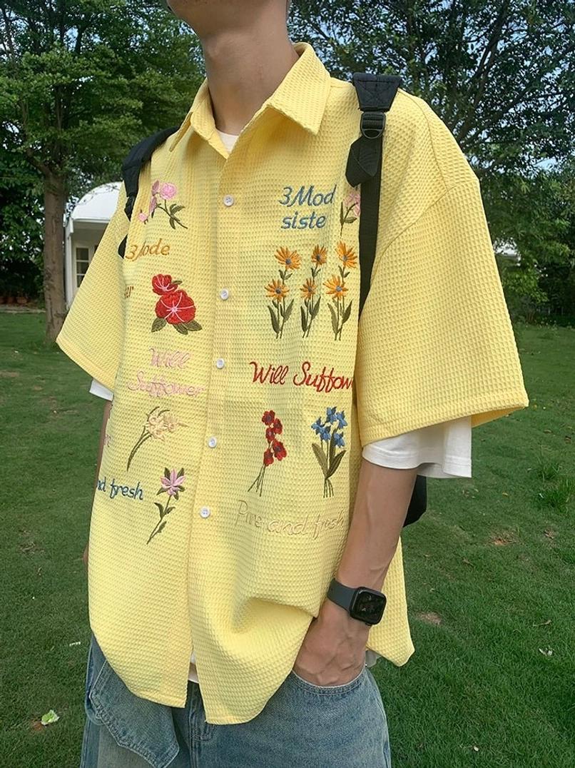 Close-up of yellow embroidered floral waffle shirt showing button front, short sleeves, textured cotton fabric, and colorful details