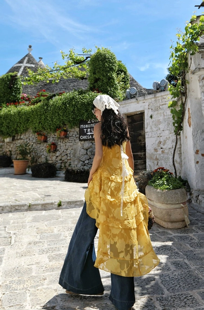 Yellow floral print boho ruffle high-low camisole top shown from the back with spaghetti straps and flowing ruffled hem on a Mediterranean village street
