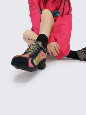 Side view of yellow patchwork streetwear platform sneakers with bear toe appliques and chunky black sculpted soles styled with black ruffled socks