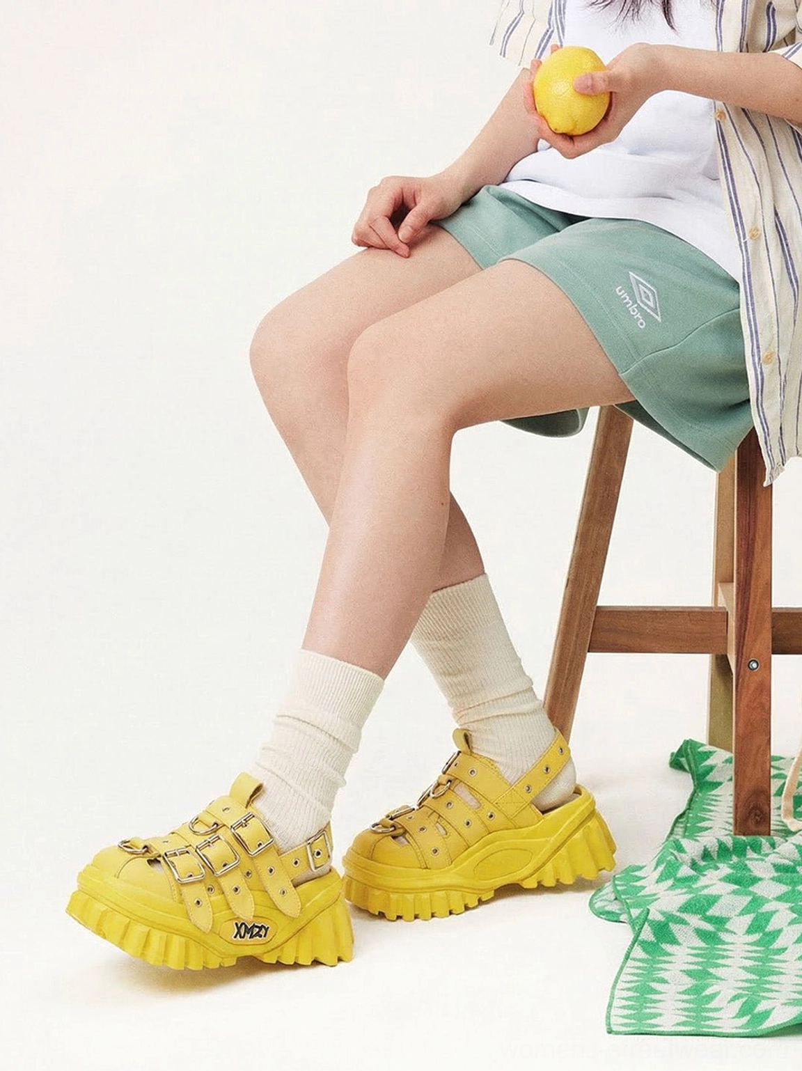 Side view of yellow punk platform sandals styled with white socks in a seated summer streetwear look