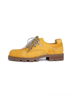 Bright yellow spotted pony hair effect leather Derby shoes with two-tone laces and chunky lug rubber sole on white background