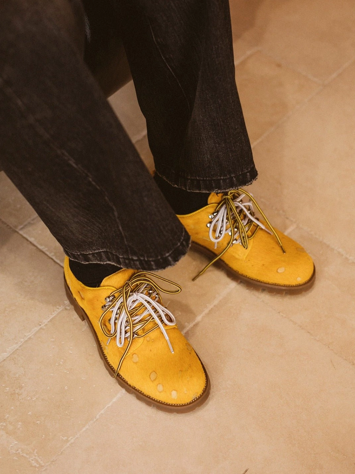 Top view of yellow spotted pony hair effect leather Derby shoes with two-tone laces worn with black jeans