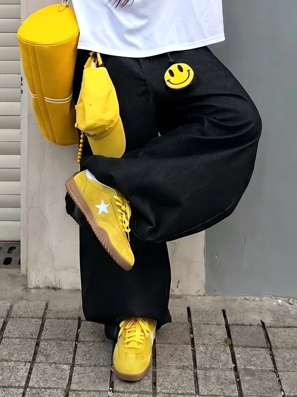 Low-angle view of yellow suede star sneakers styled with black wide-leg pants and a coordinated yellow shoulder bag