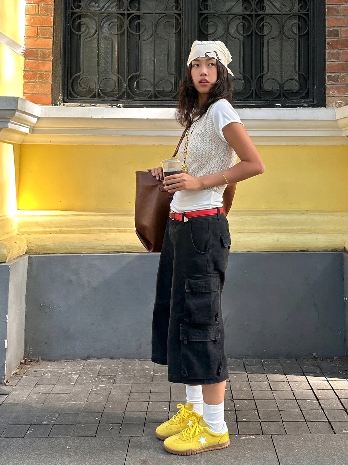 Yellow suede star trainers styled with black cropped cargo pants, a white knit top, red belt, and brown leather tote