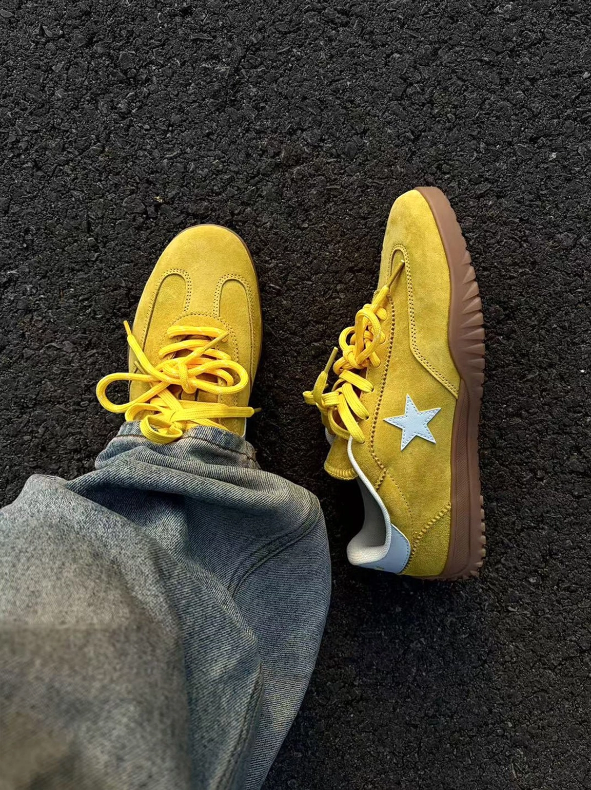 Overhead flat lay of yellow suede star trainers with white side emblems and gum soles beside blue denim jeans