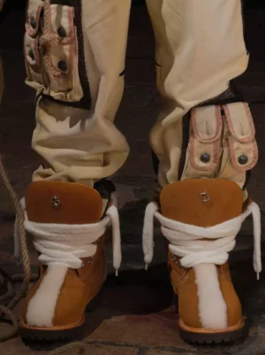 Yellow tan shearling-lined work boots worn with beige cargo pants, showing the plush fleece collar, white laces, reinforced toe detail, and rugged utility outsole