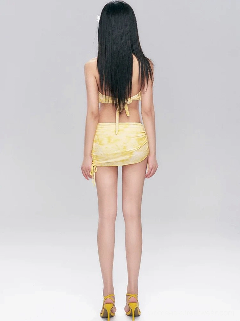 Back view of a yellow tie-dye halter swim set showing the back neck tie closure, matching ruched side drawstring skirt, and soft yellow print